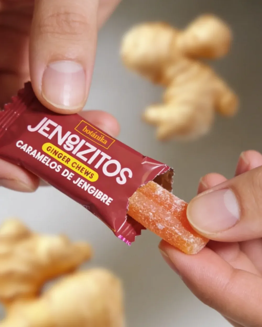 Dedos abren un caramelo de jengibre de su envoltura vino, con raíces de jengibre detrás